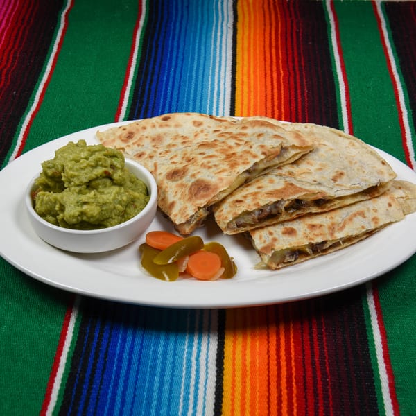 Quesadillas with guacamole and pickled vegetables on a white plate over a colorful striped serape.