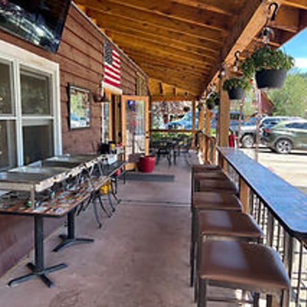 Rustic outdoor restaurant patio with a bar, stools, buffet tables, and hanging plants.