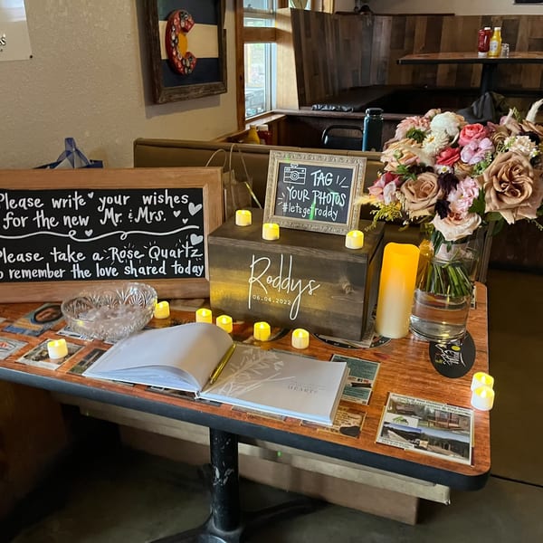 Wedding guest book table with flowers, signs, and candles in a restaurant setting.