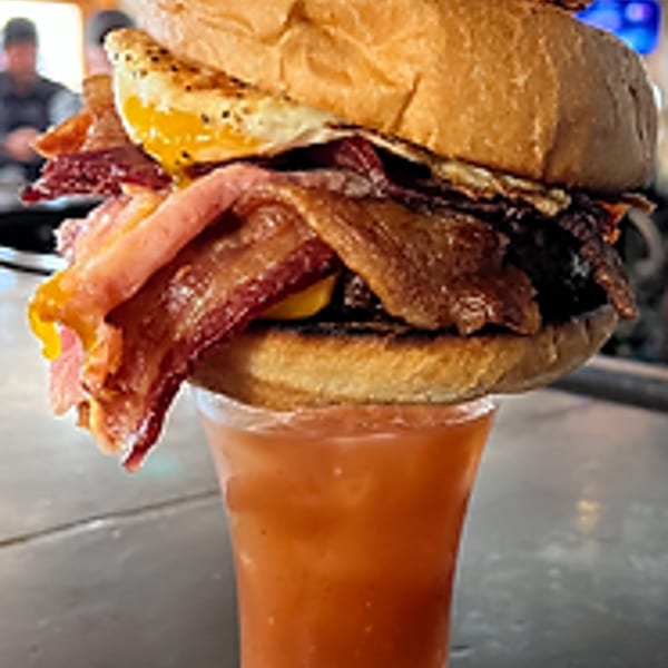 A towering Bloody Mary garnished with a burger, bacon, fried egg, and crispy bacon strips.